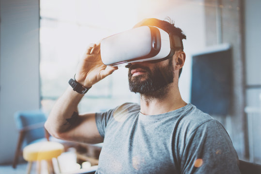 Bearded man wearing virtual reality glasses in modern interior design coworking studio. Smartphone using with VR goggles headset. Horizontal,flares effect, blurred background.