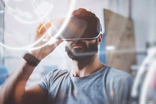 Concept of digital screen,connection and interfaces.Young beraded hipster enjoyingvirtual reality glasses in modern design home studio.Smartphone use with VR goggles headset.Horizontal,flare,blurred.