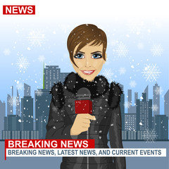 Female journalist working in winter in front of city with skyscrapers holding microphone