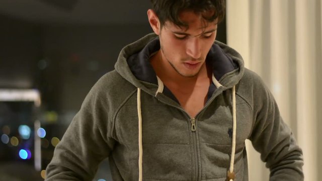 Attractive muscular young man undressing, opening sweater on naked ripped torso and removing it to reveal muscles on chest, abs, arms