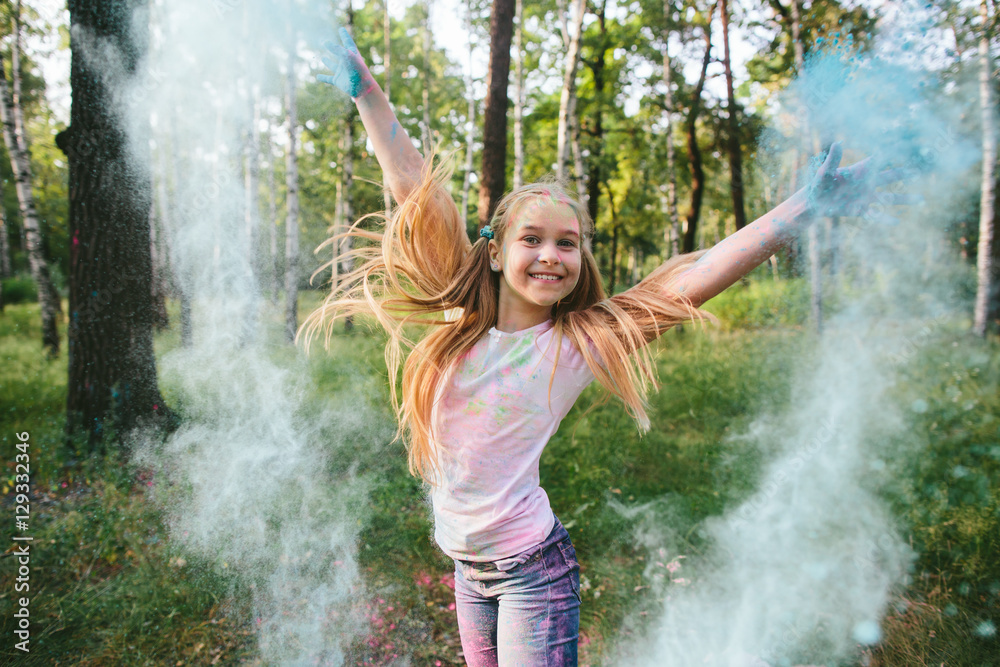 Wall mural little blonde girl in shorts and a white t-shirt in the park playing with dry paint and smiles