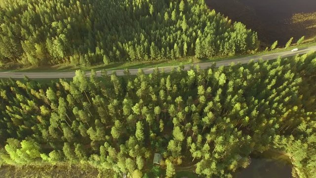 White van driving on a scenic small highway in Finnish countryside with forests and lakes. Aerial shot.