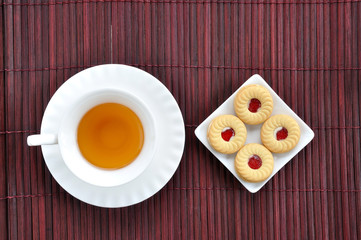 Chinese tea on brown mat with strawberry jam biscuits, top view.