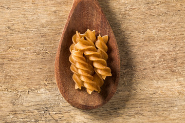 Wholemeal Fusilli into a spoon. Integral Pasta over a wooden tab