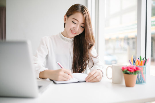 indoor picture of smiling Asia woman with notebook and pen