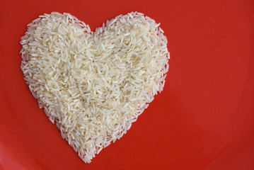 Traditionally Indian raw basmati Rice heart shape in a red plate used to make biryani or pulao , uncooked heart healthy India food 