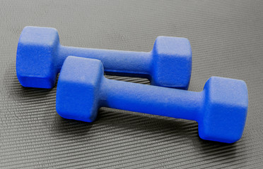 Two blue dumbbells lying on an open black exercise yoga mat