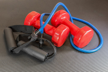 Red dumbbell weights and resistance bands lying on a black yoga