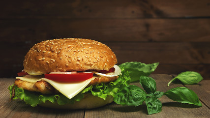 Home made hamburger with cheese, tomatoes and basil  on wooden background. Fastfood meal. Vintage toned