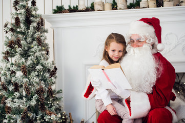 happy child girl hugging Santa reading book and laughs