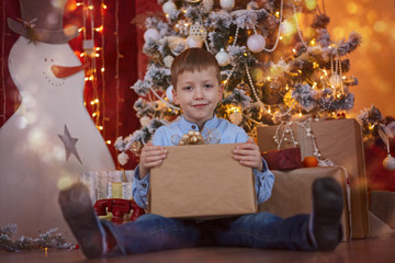 Fototapeta na wymiar Cute Little Boy opening Gift box under Christmas Tree in red house interior