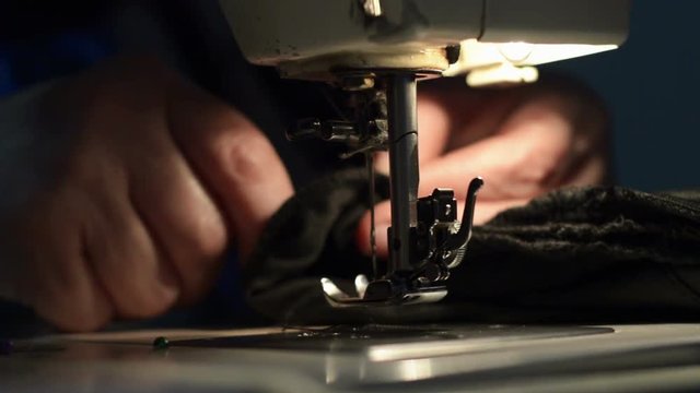 Woman using sewing machine. Woman's hands sewing cloths in low light.

