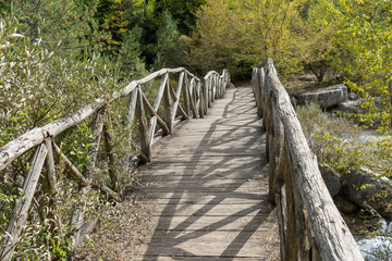 Vanishing old wooden footbridge with rails over river. Mount Olympus, Pieria, Greece.
