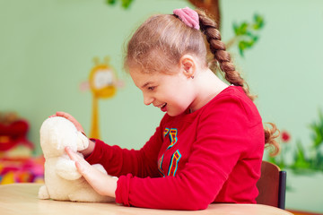 cute kid girl playing with plush toy in kindergarten for children with special need © Olesia Bilkei