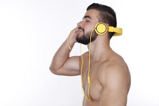 Sportlicher junger Mann mit nacktem Oberk&ouml;rper h&ouml;rt Musik mit gelben Kopfh&ouml;rern