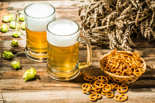Wheat spikelets with two mugs of beer with hops, pretzels on wooden table