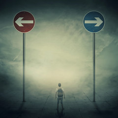 Surrealistic image as a man, with a bag in his back, stand in front of two huge road signs that...