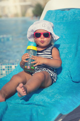 Portrait of baby drinking water on sunbed near swimming pool