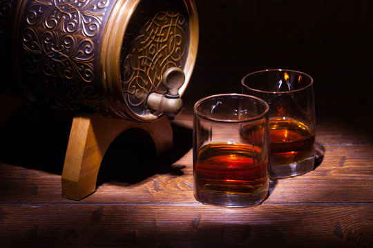 Glasses of whiskey and small barrel on wooden table