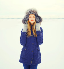 Winter fashion portrait young woman wearing a fur hat over snow