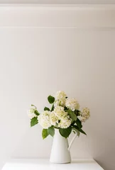 Photo sur Plexiglas Hortensia White hydrangeas in jug on table against white wall with vintage picture rail (selective focus)