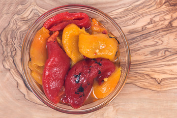 Fire roasted yellow and red peppers in bowl on olive wood cutting board