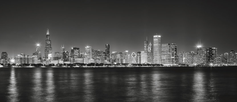 Black and white panoramic picture of Chicago city skyline with reflection in Lake Michigan at night.