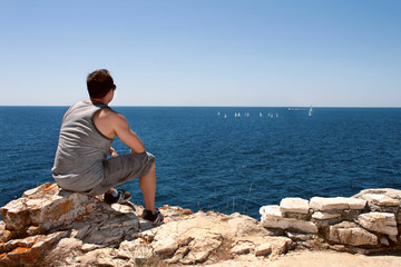 Fototapeta na wymiar He is sitting and watching the boats sailing on the sea