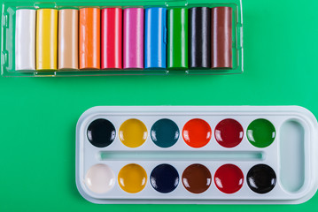 A set of children's watercolors to a set of plasticine on a green background