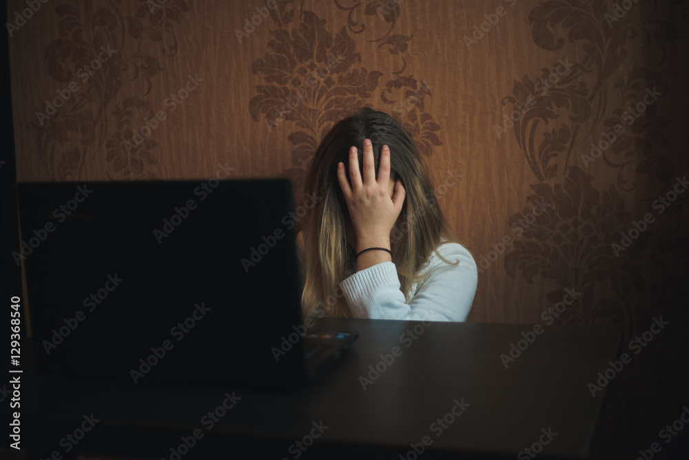 Wall mural Teen girl excessively sitting at the computer laptop at home. he is a victim of online bullying Stalker social networks