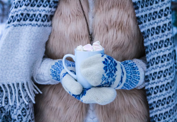Fototapeta na wymiar Woman holds cup of coffee with marshmallow in winter forest