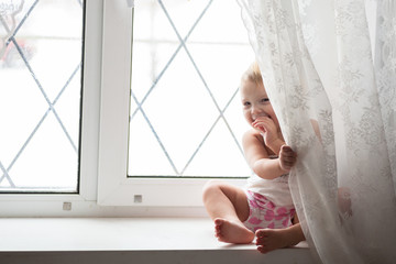 Toddler blonde girl plays on the window real interior, lifestyle