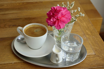 Coffee set with a cup of coffee, glass of water, milk and flower. 
