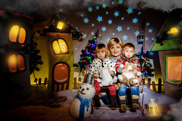 Mom with twins sitting in a winter fairy town before Christmas