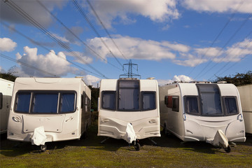 Three Caravans stored in rows on a sunny day with clouds in the sky with electricity cables in the background. Space for text. - 129375511