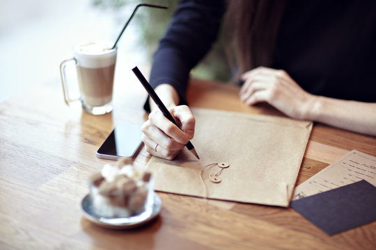 Close-up of hands, working, writing in a restaurant. Envelopes, phone, coffee, Business concept. Stationery blank layouts for design