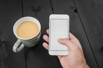 Man using smartphone, close-up, cup of coffee and on the balck wooden background. Top view.