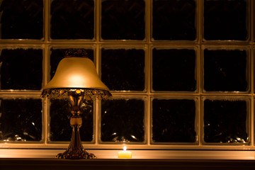 A candle lit lamp casting a golden glow against a frosted multi square paned window