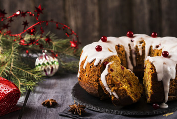 Christmas homemade cake with nuts, apples and cranberries with icing on dark wooden background. Selective focus 