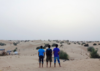 A group of 3 young Indian men watching the sunset at a desert safari camp in Dubai, UAE