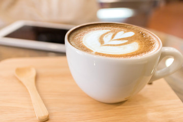 Cup of coffee with heart pattern in a white cup on wooden background