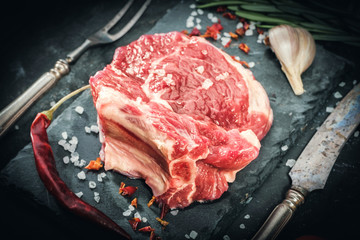 Raw beef steak with salt and herbs on stone cutting board.