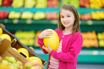Fototapeta na wymiar Little girl choosing a melon in a food store or a supermarket