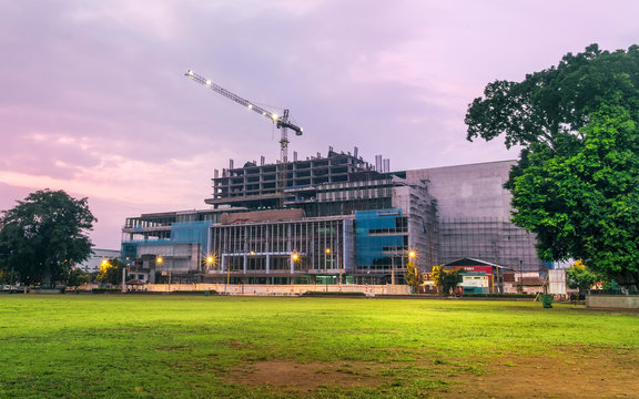 High building construction progress, captured from far away at dawn. Featuring tall crane, with safety lamp still light up