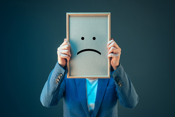 Businesswoman is pessimistic, holding smiley emoticon over face - obrazy, fototapety, plakaty