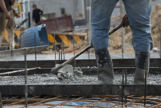 Concrete casting work.Worker wearing blue jeans and plastic brown boots leveling concrete work step of the building construction.