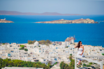 Fototapeta na wymiar BYoung lady relaxing on the edge of swimming pool with beautiful view of amazing greek village