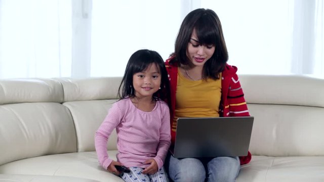 Young woman working with a laptop computer on the sofa while her daughter watching television at home