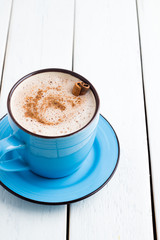 Cocoa in a blue cup with cinnamon stick on a white background
