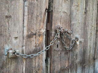 Picture of an old wooden gate closed with rusty chain. Background of the old batten door. Rusty padlock on the old door. An old planking of the gate.